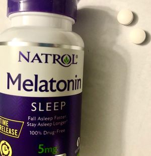 Two round white melatonin tablets next to a bottle of melatonin tablets.